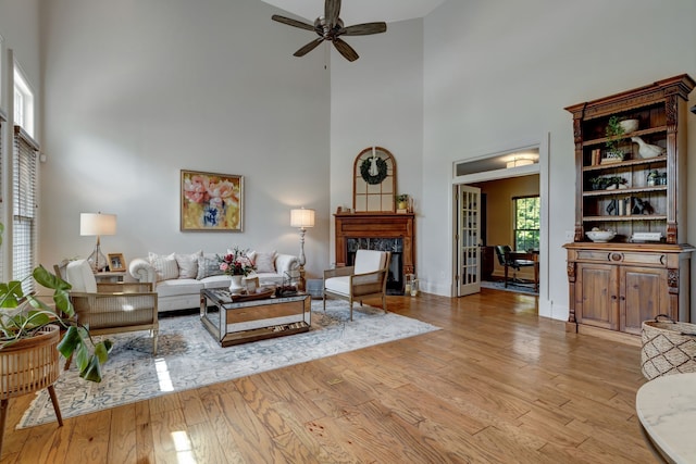 living room with a fireplace, a towering ceiling, light wood-type flooring, and ceiling fan