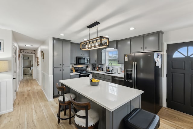 kitchen with a center island, hanging light fixtures, gray cabinets, light wood-type flooring, and stainless steel appliances