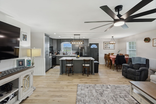 living room with sink, ceiling fan with notable chandelier, and light wood-type flooring