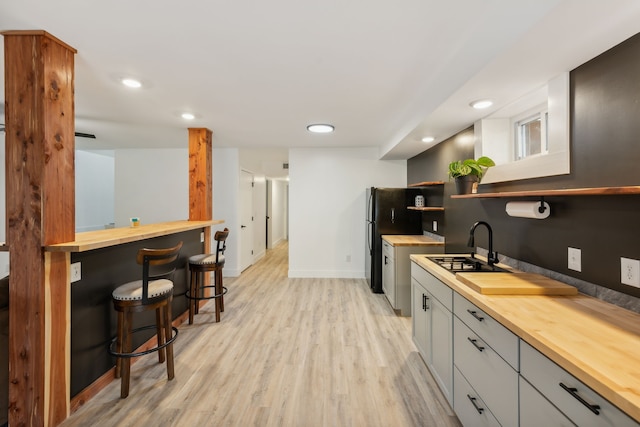 kitchen featuring gray cabinetry, wooden counters, a kitchen breakfast bar, black fridge, and light hardwood / wood-style floors