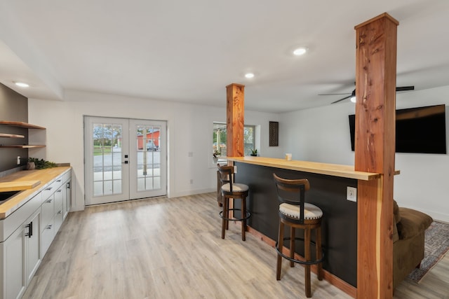 kitchen with french doors, light wood-type flooring, a breakfast bar, white cabinets, and butcher block counters