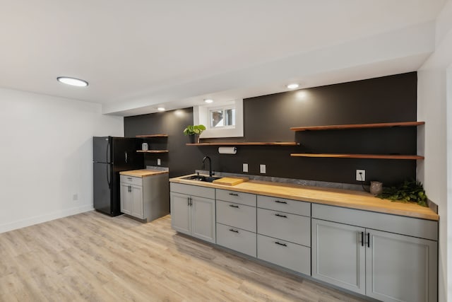 kitchen featuring light wood-type flooring, black fridge, gray cabinetry, sink, and butcher block counters