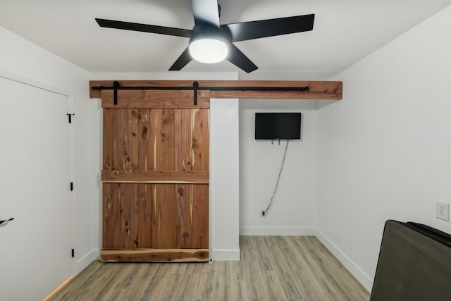 unfurnished bedroom featuring light wood-type flooring, a barn door, and ceiling fan