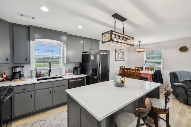 kitchen with sink, a center island, stainless steel appliances, decorative light fixtures, and light wood-type flooring