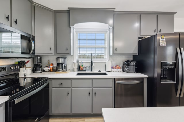 kitchen featuring gray cabinetry, sink, light hardwood / wood-style flooring, appliances with stainless steel finishes, and tasteful backsplash