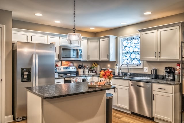 kitchen with stainless steel appliances, sink, light hardwood / wood-style flooring, a kitchen island, and hanging light fixtures