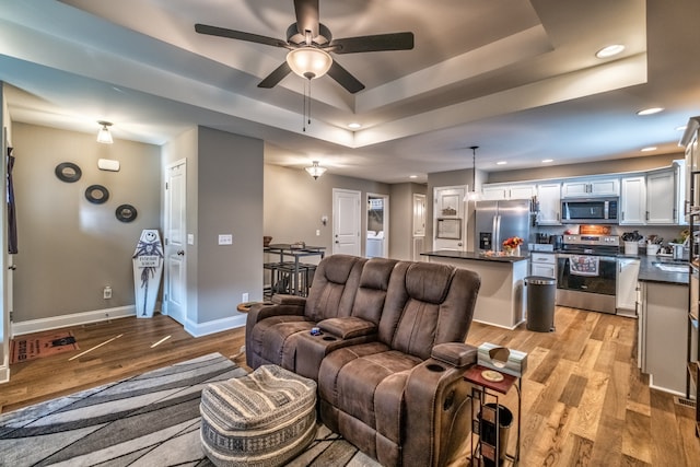 living room featuring ceiling fan, light hardwood / wood-style floors, sink, and a tray ceiling