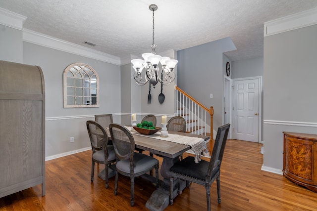 dining area with a textured ceiling, light hardwood / wood-style floors, an inviting chandelier, and crown molding