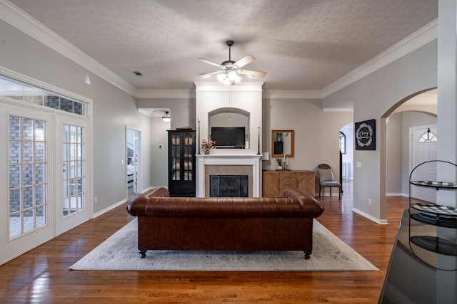 living room featuring a textured ceiling, a tiled fireplace, crown molding, and dark hardwood / wood-style floors