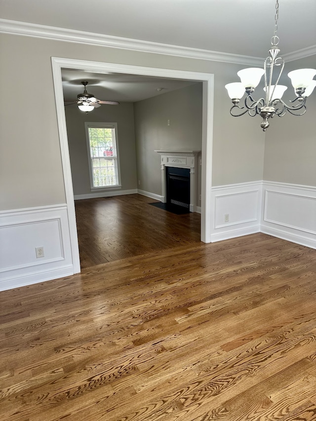 unfurnished dining area featuring crown molding, ceiling fan with notable chandelier, and dark hardwood / wood-style floors