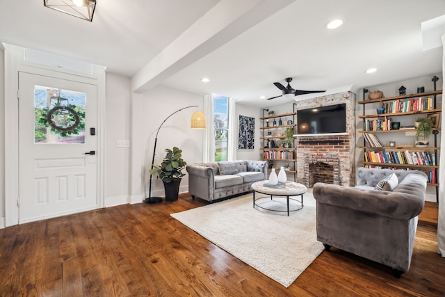 living room with beam ceiling, ceiling fan, a fireplace, and dark wood-type flooring