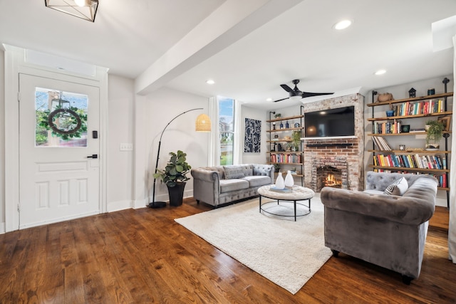 living room featuring ceiling fan, beam ceiling, dark hardwood / wood-style flooring, and a fireplace