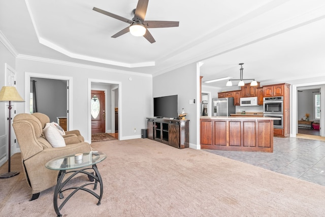 carpeted living room featuring a raised ceiling, ceiling fan, and ornamental molding