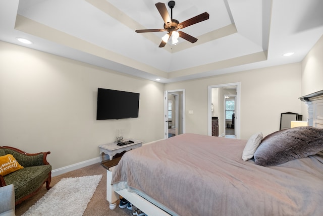 bedroom featuring light colored carpet, a raised ceiling, ceiling fan, and ensuite bathroom