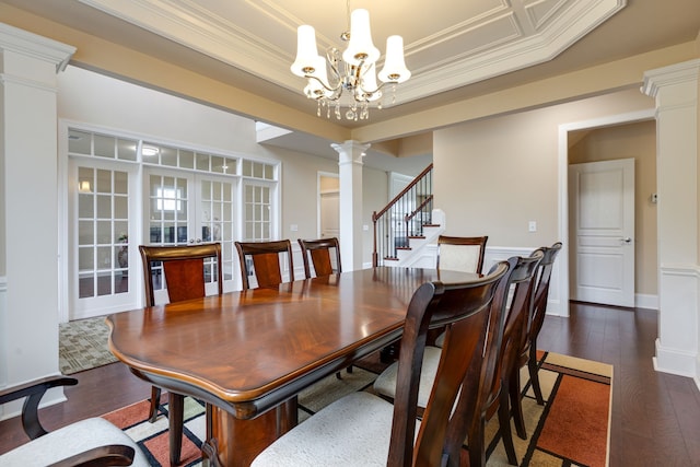 dining area with a raised ceiling, dark hardwood / wood-style floors, ornamental molding, a notable chandelier, and decorative columns