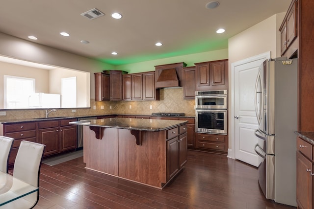 kitchen featuring appliances with stainless steel finishes, a center island, dark wood-type flooring, and sink