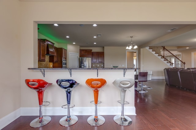 kitchen featuring dark stone counters, a kitchen breakfast bar, dark hardwood / wood-style floors, kitchen peninsula, and stainless steel appliances