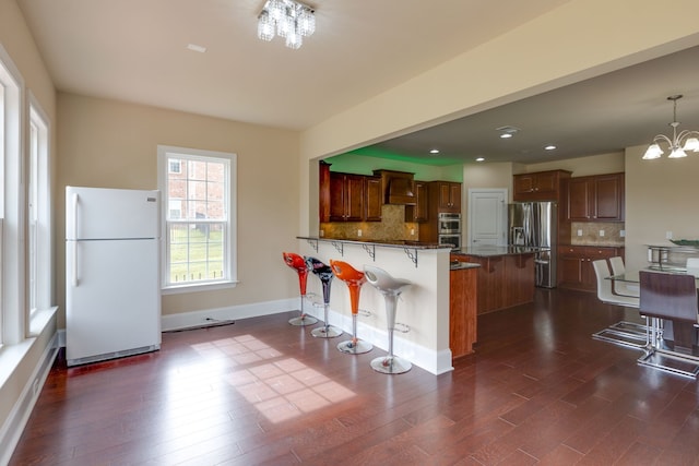 kitchen featuring dark wood-type flooring, an inviting chandelier, appliances with stainless steel finishes, a kitchen bar, and custom range hood