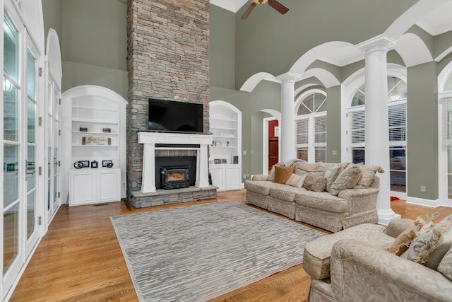 living room with a towering ceiling, ornate columns, ceiling fan, built in features, and light hardwood / wood-style floors