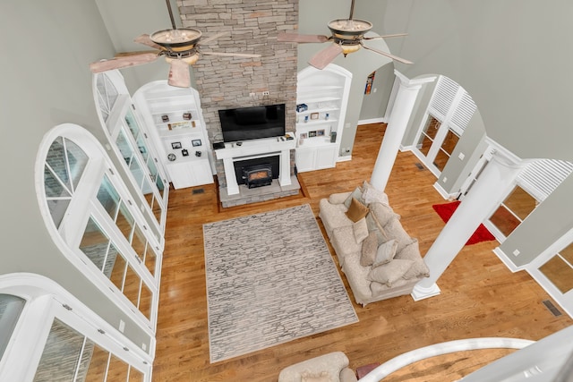 living room featuring a stone fireplace, hardwood / wood-style flooring, ceiling fan, a towering ceiling, and decorative columns