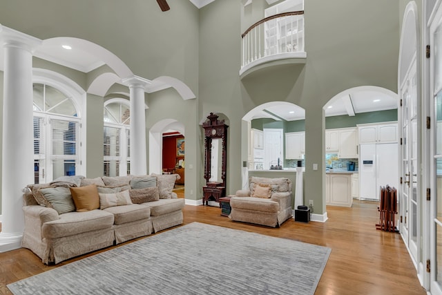 living room with decorative columns, light hardwood / wood-style flooring, a towering ceiling, and ornamental molding