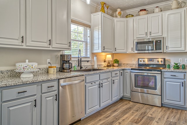 kitchen with sink, ornamental molding, a textured ceiling, appliances with stainless steel finishes, and light hardwood / wood-style floors