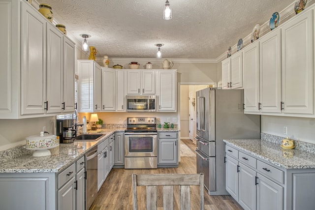 kitchen with sink, light wood-type flooring, ornamental molding, a textured ceiling, and appliances with stainless steel finishes