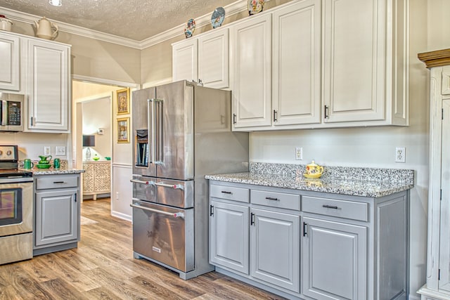 kitchen with ornamental molding, a textured ceiling, appliances with stainless steel finishes, light hardwood / wood-style floors, and light stone counters