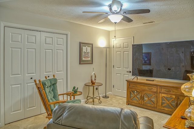 living area with ceiling fan, light colored carpet, and a textured ceiling