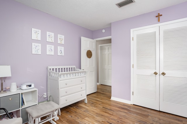 bedroom featuring a crib, a textured ceiling, hardwood / wood-style flooring, and a closet