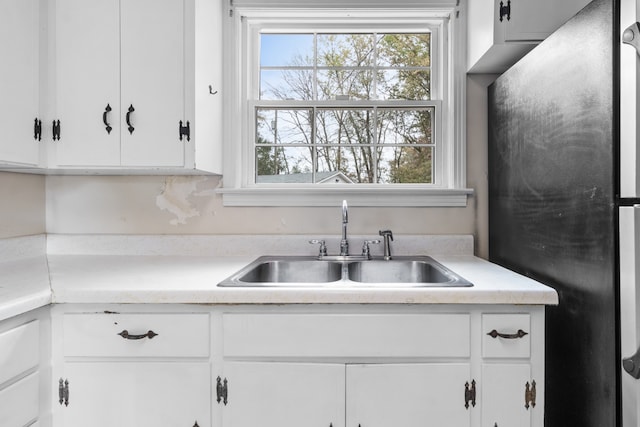 kitchen featuring sink, white cabinets, and fridge