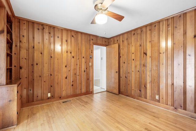 empty room with light hardwood / wood-style flooring, ceiling fan, wooden walls, and crown molding