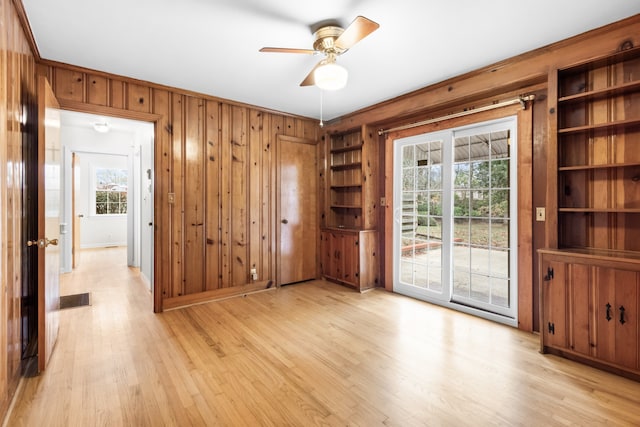 spare room with light wood-type flooring, plenty of natural light, wood walls, and ceiling fan