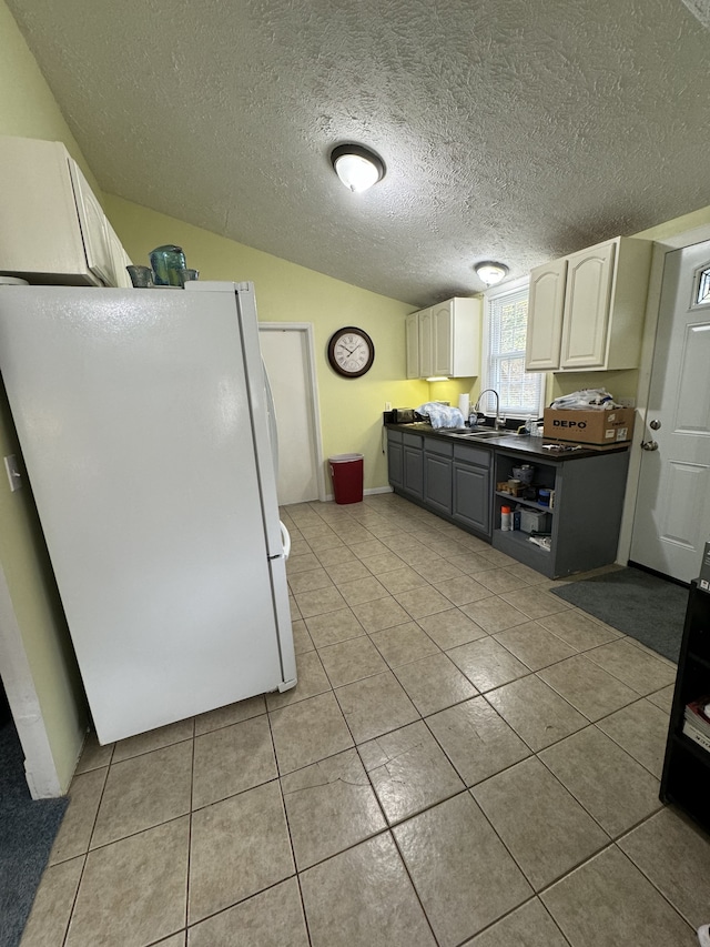 kitchen featuring a textured ceiling, sink, white cabinets, white fridge, and light tile patterned flooring