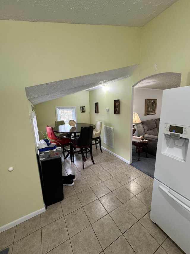 dining area featuring light tile patterned floors, a textured ceiling, and lofted ceiling