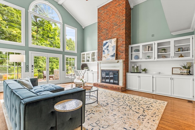 living room featuring a fireplace, high vaulted ceiling, light hardwood / wood-style flooring, and ornamental molding