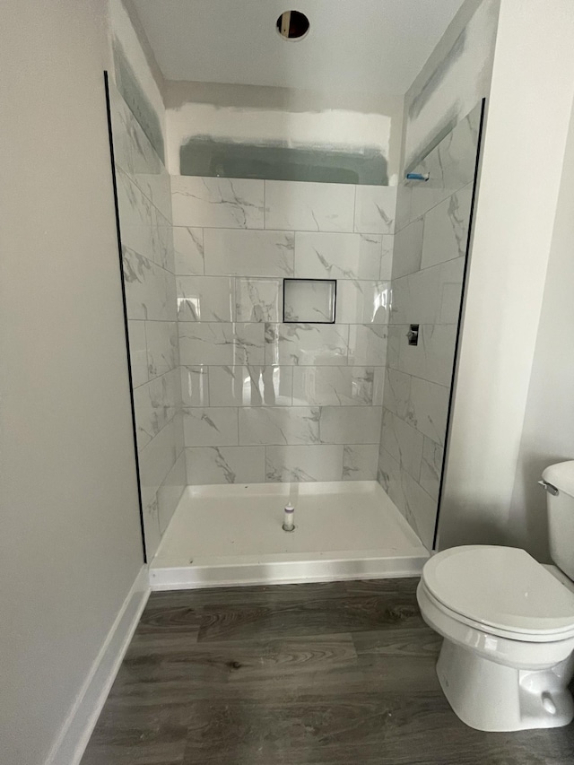 bathroom with tiled shower, wood-type flooring, and toilet