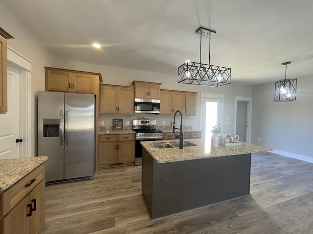 kitchen with a sink, stainless steel appliances, light stone counters, and wood finished floors