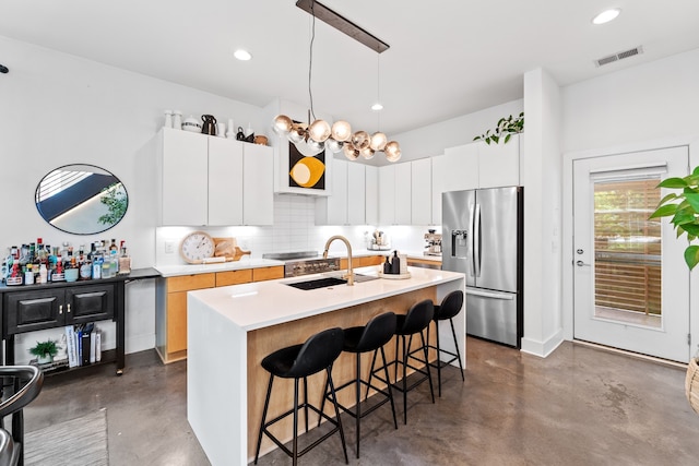 kitchen featuring white cabinets, stainless steel refrigerator with ice dispenser, a kitchen bar, and a center island with sink