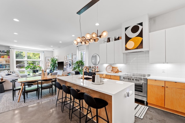 kitchen with white cabinets, concrete flooring, stainless steel range with electric stovetop, and an island with sink