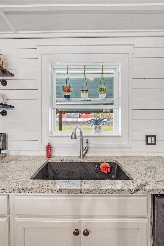 kitchen with plenty of natural light, wood walls, light stone countertops, and sink