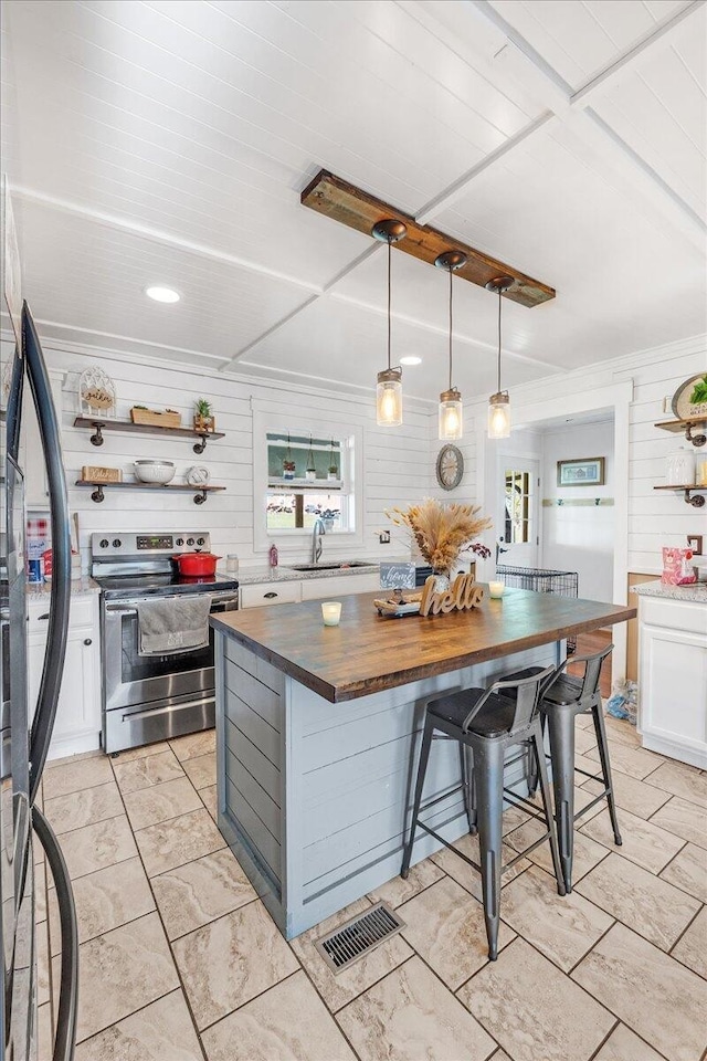 kitchen with stainless steel electric range oven, wooden counters, decorative light fixtures, a breakfast bar, and white cabinets