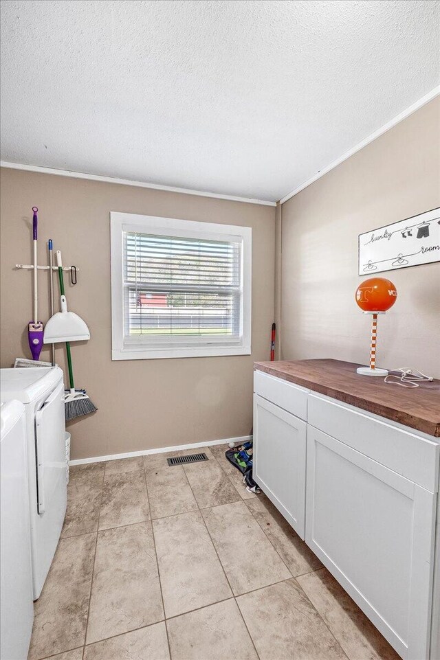 laundry area featuring cabinets, a textured ceiling, crown molding, washing machine and clothes dryer, and light tile patterned flooring