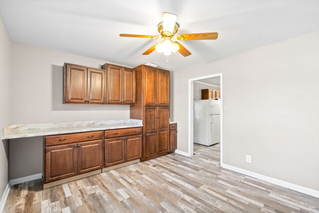 kitchen featuring ceiling fan, white fridge, built in desk, and light wood-type flooring