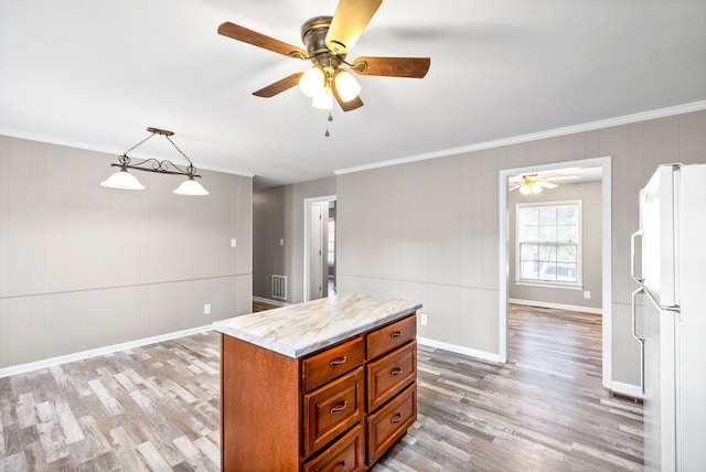 kitchen with light stone countertops, light wood-type flooring, ornamental molding, pendant lighting, and white fridge