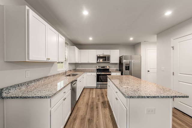 kitchen featuring light wood-type flooring, stainless steel appliances, sink, white cabinets, and a center island