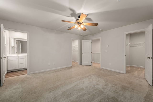 unfurnished bedroom featuring light carpet, a walk in closet, ceiling fan, sink, and connected bathroom