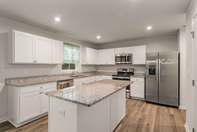 kitchen featuring light wood-type flooring, light stone counters, stainless steel appliances, a center island, and white cabinetry