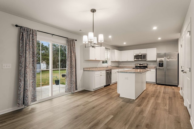 kitchen with white cabinetry, hanging light fixtures, light hardwood / wood-style floors, a kitchen island, and appliances with stainless steel finishes