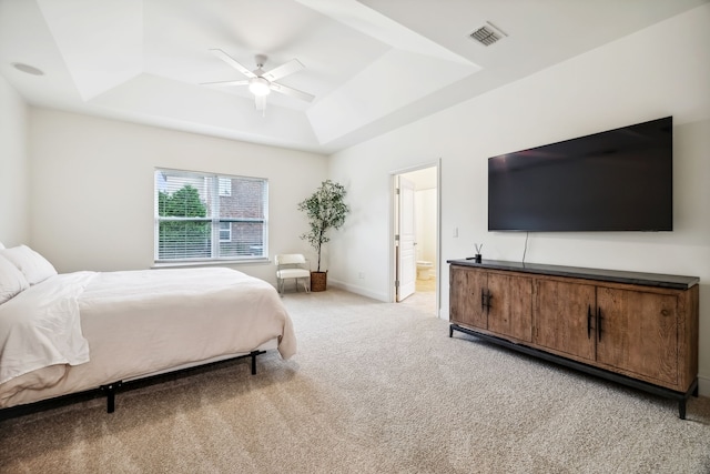 bedroom with ensuite bathroom, ceiling fan, a raised ceiling, and light colored carpet